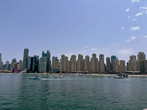 Modern city skyline with tall skyscrapers by the sea and boats on the water under a clear blue sky, urban waterfront cityscape on a sunny day