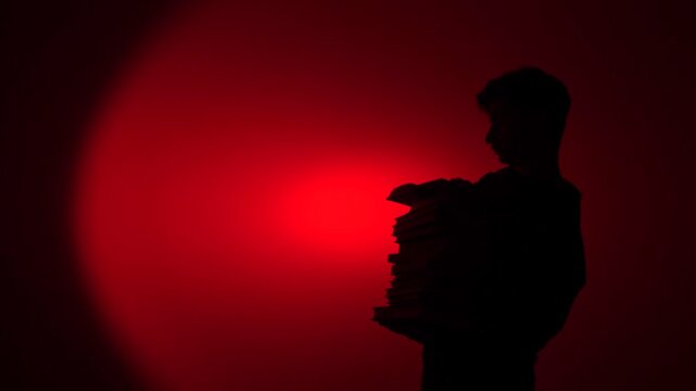 Person silhouette holding stack of books in red light