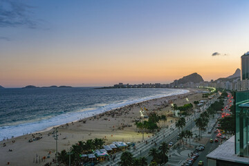 Fototapeta premium The breathtaking sunset over Copacabana Beach paints the sky with vibrant hues of orange and pink, reflecting on the Atlantic Ocean and illuminating Rio’s iconic skyline.