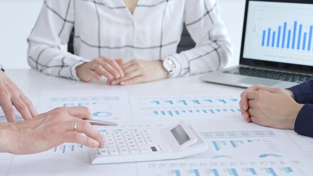 Business people professionals or accouters analyzing financial reports, charts and graphs on laptop and paper, using calculator to discuss strategy, budgeting and teamwork decisions