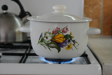 Vintage Enamel Cooking Pot with Floral Design Heating on a Gas Stove Burner with a Blue Flame, Representing Traditional Home Cooking