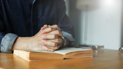 Obraz premium Close up of man hands clasped together on an open book, symbolizing faith, hope, and mindfulness for concepts of prayer, meditation, reflection, spiritual study, or inner peace in daily life concept