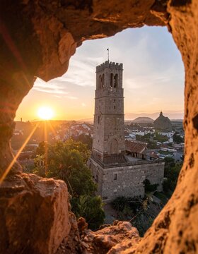 Historic stone tower at sunset framed by a rough aperture, town below