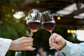 Close up of a couple's hands toasting with glasses of red wine at an outdoor restaurant. Celebration, anniversary, or romantic date night concept. Cheers!