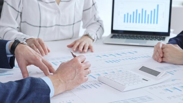 Business people professionals or accouters analyzing financial reports, charts and graphs on laptop and paper, using calculator to discuss strategy, budgeting and teamwork decisions