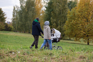 Couple with baby pram walking in city park in autumn