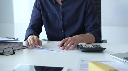 Professional businessman calculating financial data, reviewing documents near laptop in modern workplace setting. Audit and taxes, business concept - Powered by Adobe
