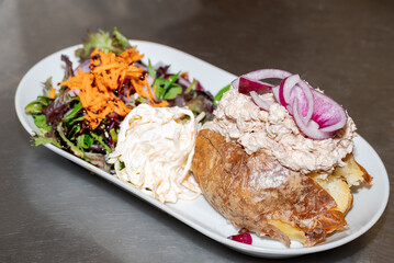 Enjoying a baked potato lunch! Topped with tuna and red onion, served with coleslaw and a fresh salad. A tasty and satisfying meal.