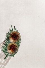 Transparent alcohol Glasses with dark shadows at sunlight on beige table, green palm leaf decoration, top view minimal photo, aesthetic flat lay shiny glass at natural light, summer strong drink
