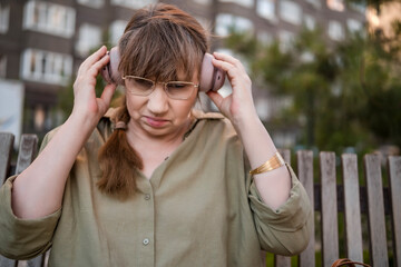 Elderly woman puts on headphones, draws in notebook, pursues hobby, sitting on bench in city park. Active age, interesting life and creative abilities of older people