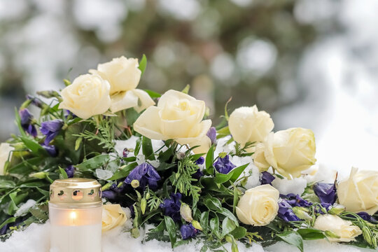 A beautiful memorial bouquet of blue and white flowers on a snowy winter day in a cemetery. Funeral flowers in the winter frost. A burning candle and a flower arrangement on the snowy ground.