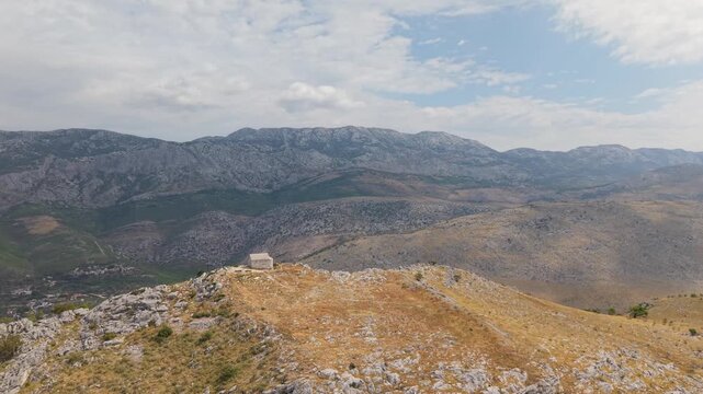 Ancient stone chapel on a coastal mountain ridge with panoramic sea view of the Dalmatian coast.