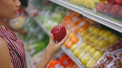 Young woman selects red apple supermarket shelf, young woman holds fresh fruit display with lemons oranges, hand chooses vibrant produce, healthy grocery moment, perfect lifestyle videos fresh eating.