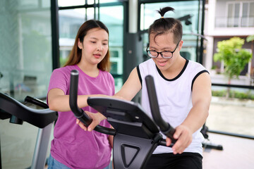 A young woman assisting a man with down syndrome exercising on fitness equipment © offsuperphoto