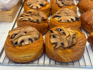 Golden layered pastries topped with sliced mushrooms on rack. Bakery products, food photography, and traditional baked goods.