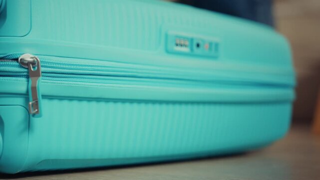 Person Closing Blue Suitcase Before Travel on Wooden Floor