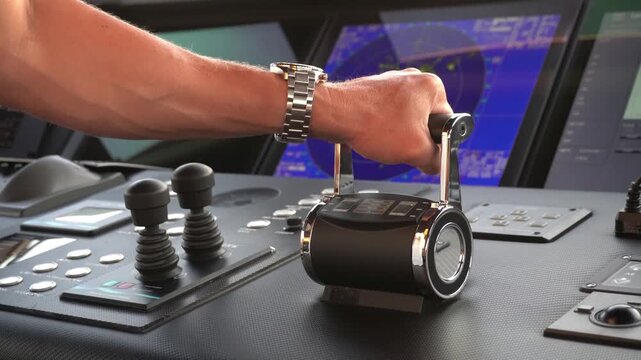 Close-up of a captain&rsquo;s hand operating engine throttle controls on a ship bridge with radar screens and navigation equipment on background. Maritime technology and vessel operation at sea. Full astern