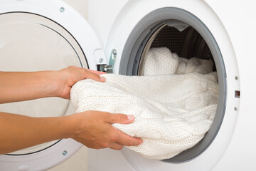 Young adult woman hands holding and unloading white warm soft sweater from opened washing machine....