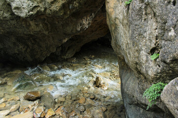 A clear mountain stream flows through a rocky cave in Swat, Pakistan, surrounded by natural stone formations and lush green ferns.