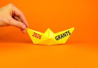 2026 Grants symbol. Concept words 2026 Grants on beautiful yellow paper boat. Beautiful orange paper background. Businessman's hand. Business and 2026 grants concept. Copy space.