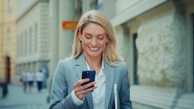 Smiling Businesswoman Using Smartphone While Walking in City