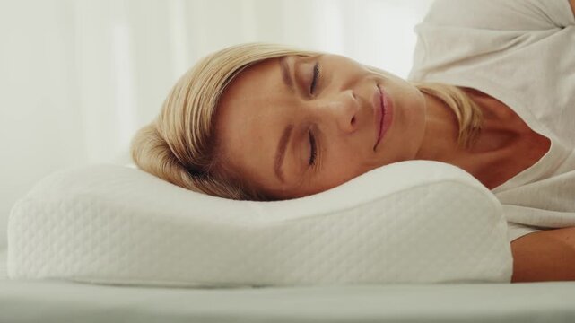 Woman peacefully sleeping on ergonomic pillow in bright bedroom
