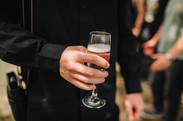 A male businessman holds a glass of champagne in his hand at a party during the day.