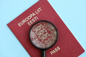Estonia passport and magnifying glass on light blue paper. Citizenship details and information