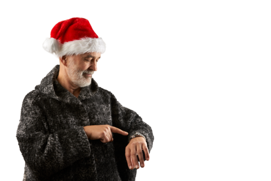A senior citizen wearing a Santa Claus hat points to the time on his wristwatch with his index finger. Png.