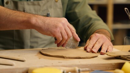 Unrecognizable Caucasian skilled man guy small business owner businessman crock potter ceramist artisan male hands cutting clay material using tools equipment making pottery ceramic indoors workshop