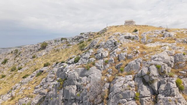 Ancient stone chapel on a coastal mountain ridge with panoramic sea view of the Dalmatian coast.