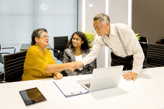 Diverse businesspeople discussing during working at laptop computer together. Senior mature Asian manager has a handshake with coworkers at office. Successful business team brainstorming in a meeting.