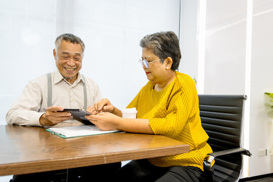 Two senior businesspeople working together. Elderly Asian businesswoman holding tablet while discussing with senior manager at office. Happy successful mature business team brainstorming in a meeting.