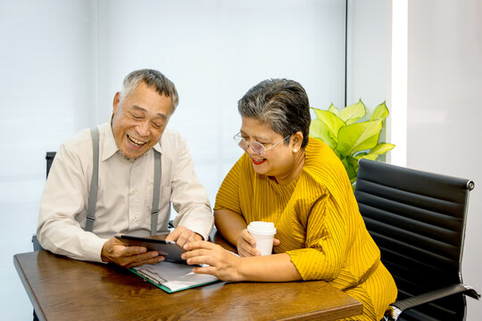 Two senior businesspeople working together. Elderly Asian businesswoman holding tablet while discussing with senior manager at office. Happy successful mature business team brainstorming in a meeting.