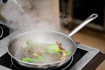 Fresh spinach and mushrooms sautéing in a steaming pan on a modern stovetop, with liquid being poured during cooking. High heat, healthy ingredients, and culinary action captured.