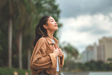 Carefree asian woman standing in city park enjoying fresh air and nature – happy female smiling...