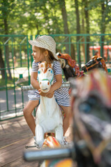 Funny laughing little girl in a hat rides on a merry-go-round hugging a horse