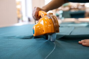 A cutter or pattern cutter uses an electric rotary cutter to cut through a stack of fabric in a garment factory. A concept of the textile industry and mass production.