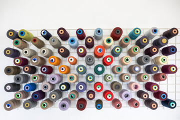 Spools of thread of various colors neatly arranged on wooden shelves, creating a visually appealing display for sewing and tailoring projects or facilities.
