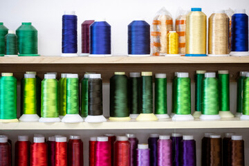 Spools of thread of various colors neatly arranged on wooden shelves, creating a visually appealing display for sewing and tailoring projects or facilities.