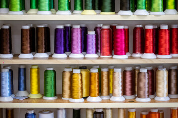 Spools of thread of various colors neatly arranged on wooden shelves, creating a visually appealing display for sewing and tailoring projects or facilities.