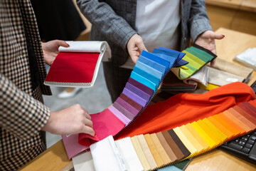 Two designers or a client and a decorator collaborating on a project. They are choosing from a variety of colorful fabric swatches for fashion or interior design.