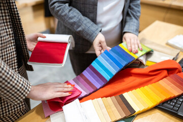 Two designers or a client and a decorator collaborating on a project. They are choosing from a variety of colorful fabric swatches for fashion or interior design.