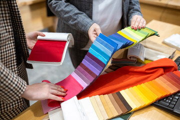Two designers or a client and a decorator collaborating on a project. They are choosing from a variety of colorful fabric swatches for fashion or interior design.