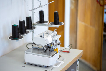 A professional overlock sewing machine, or serger, with black thread spools in a garment factory. A concept of the textile industry, tailoring, and clothing production.