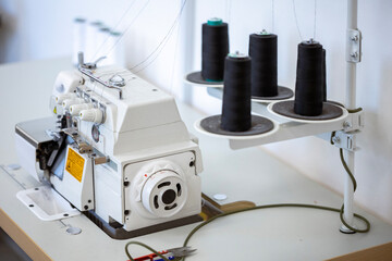 A professional overlock sewing machine, or serger, with black thread spools in a garment factory. A concept of the textile industry, tailoring, and clothing production.