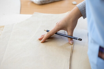 A fashion designer, cutter, or dressmaker working with paper sewing patterns on a large table. A...