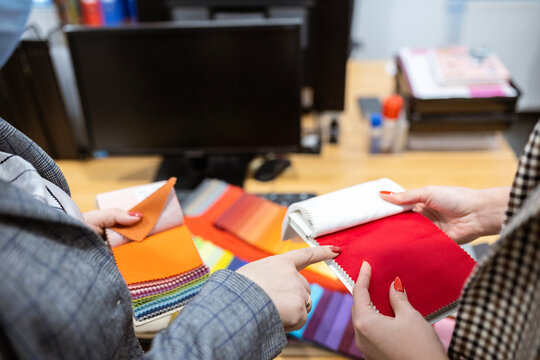 Two designers or a client and a decorator collaborating on a project. They are choosing from a variety of colorful fabric swatches for fashion or interior design.