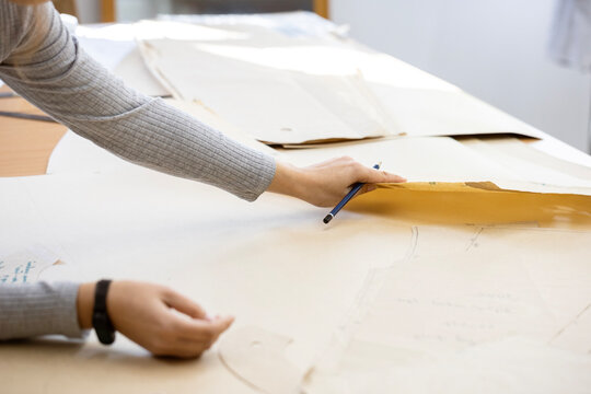 A fashion designer, cutter, or dressmaker working with paper sewing patterns on a large table. A concept of the creative process and handmade clothing design. - Powered by Adobe
