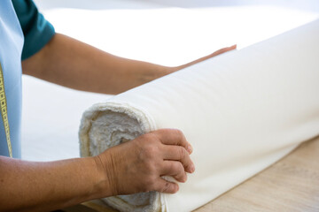 Hands of a cutter unrolling a large bolt of white fabric on a cutting table in a garment factory. Preparing the material for sewing and clothing production.